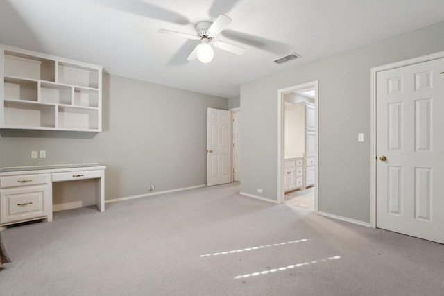 interior space with ceiling fan, built in desk, light colored carpet, and ensuite bath