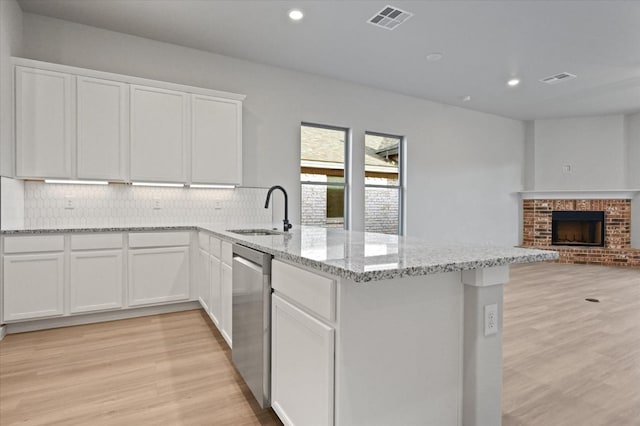 kitchen with sink, dishwasher, white cabinetry, light stone countertops, and kitchen peninsula