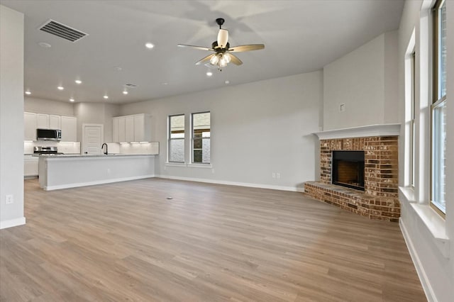 unfurnished living room featuring ceiling fan, a brick fireplace, sink, and light wood-type flooring