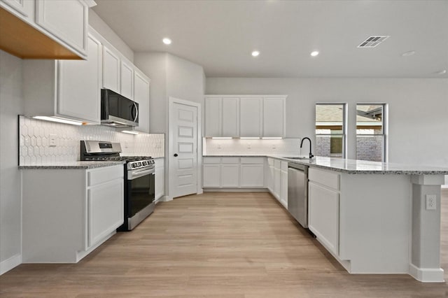 kitchen featuring sink, stainless steel appliances, light stone counters, white cabinets, and kitchen peninsula