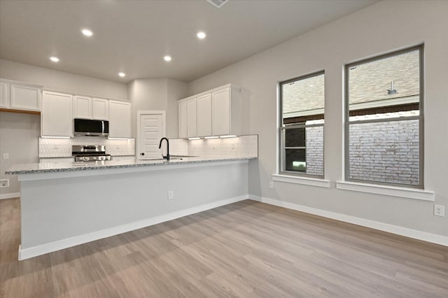 kitchen with white cabinetry, appliances with stainless steel finishes, kitchen peninsula, and light stone counters