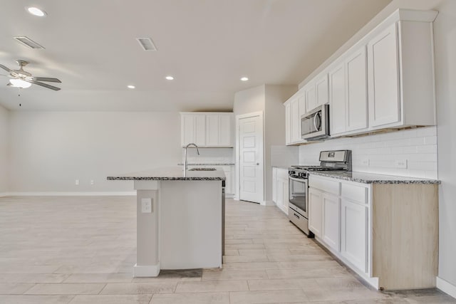 kitchen featuring white cabinets, appliances with stainless steel finishes, and dark stone counters