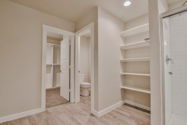 bathroom with wood-type flooring, tiled shower, and toilet