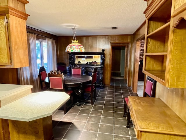 dining space with dark tile patterned floors, a textured ceiling, and wood walls