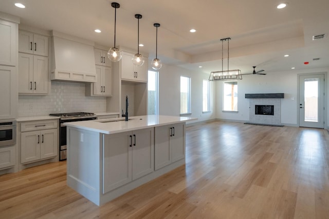 kitchen with sink, hanging light fixtures, gas range, custom range hood, and a center island with sink