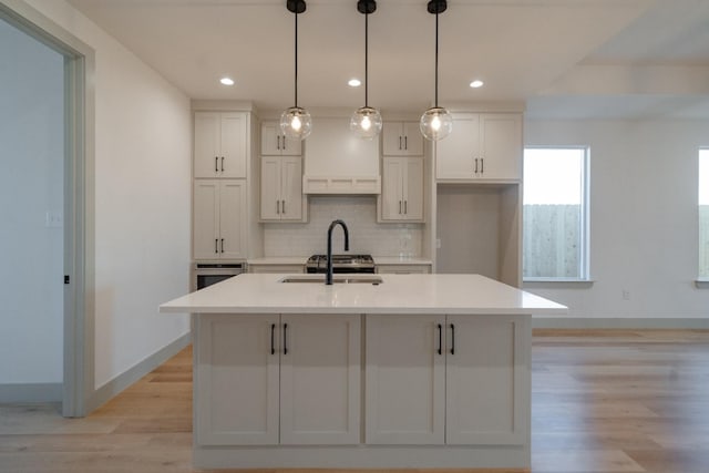 kitchen featuring sink, white cabinetry, hanging light fixtures, a kitchen island with sink, and decorative backsplash