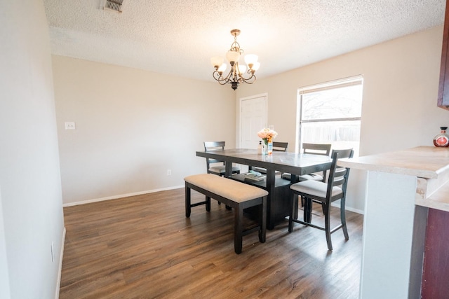 dining room featuring dark wood-type flooring, a textured ceiling, and a notable chandelier