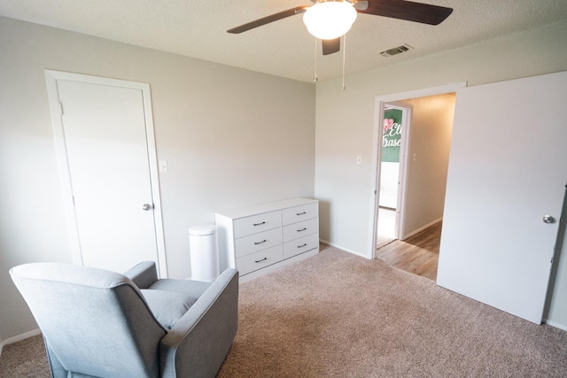 living area featuring ceiling fan, light carpet, and a textured ceiling