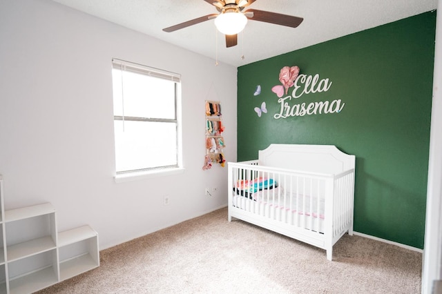 bedroom featuring a nursery area, carpet, and ceiling fan