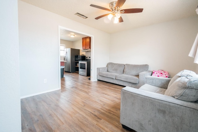 living room featuring ceiling fan, light hardwood / wood-style flooring, and a textured ceiling