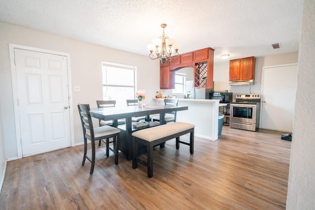 dining room featuring an inviting chandelier, a textured ceiling, and light wood-type flooring