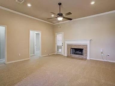 unfurnished living room featuring light carpet, crown molding, a fireplace, and ceiling fan