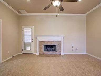 unfurnished living room featuring ornamental molding, carpet floors, ceiling fan, and a fireplace