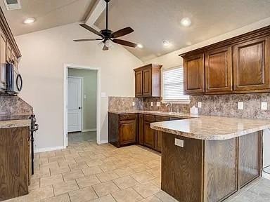 kitchen featuring vaulted ceiling with beams, light stone counters, kitchen peninsula, ceiling fan, and decorative backsplash