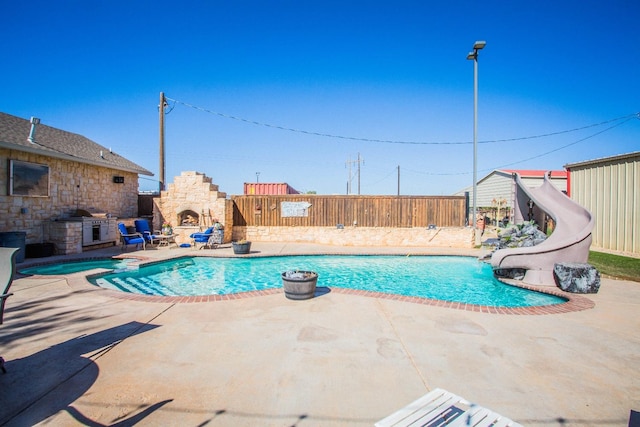 view of swimming pool featuring an outdoor kitchen, an outdoor stone fireplace, and a patio area