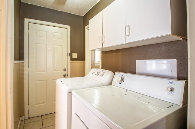 laundry room with cabinets, light tile patterned floors, a textured ceiling, and washer and clothes dryer