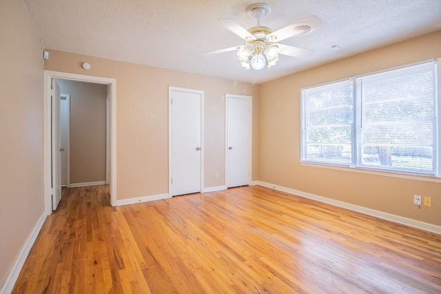 unfurnished bedroom with ceiling fan, light hardwood / wood-style flooring, and multiple closets