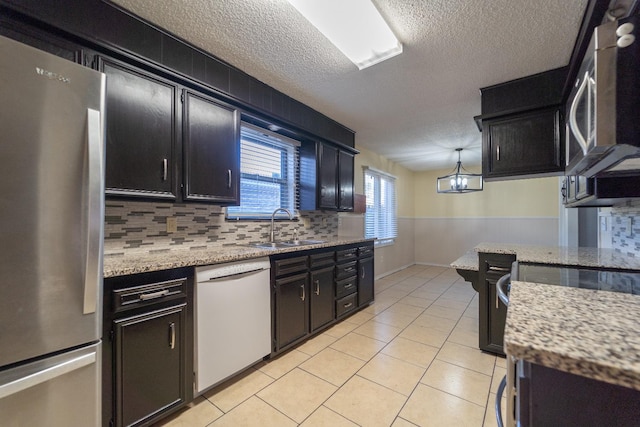 kitchen with sink, decorative light fixtures, light tile patterned floors, stainless steel appliances, and light stone countertops