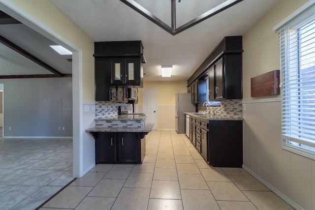 kitchen featuring sink, light tile patterned floors, stainless steel appliances, light stone countertops, and a kitchen bar