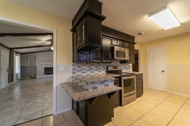 kitchen featuring vaulted ceiling with beams, light stone counters, a brick fireplace, a textured ceiling, and stainless steel appliances