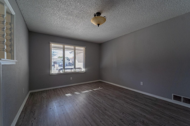 spare room featuring dark wood-type flooring and a textured ceiling