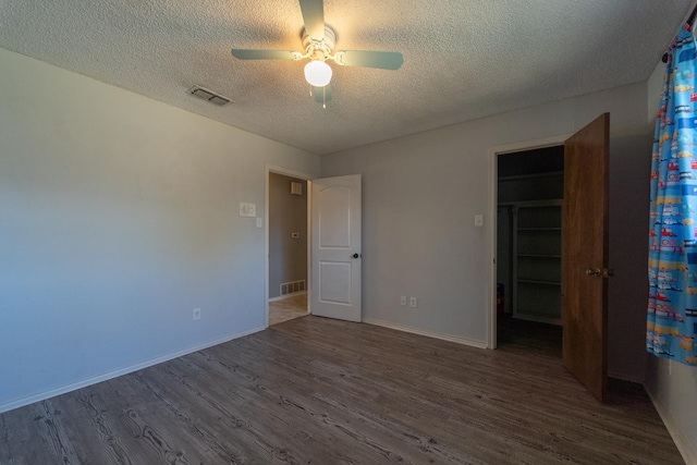 unfurnished bedroom with hardwood / wood-style flooring, a spacious closet, ceiling fan, a textured ceiling, and a closet