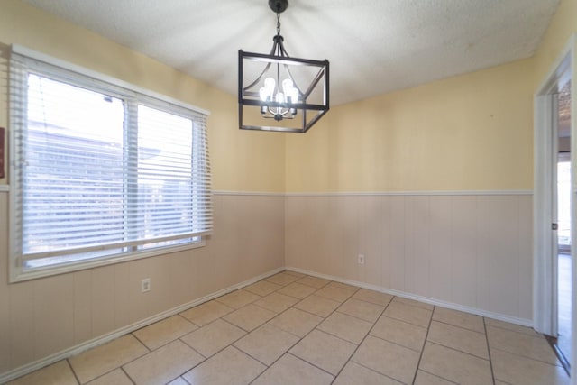 unfurnished dining area with an inviting chandelier, a textured ceiling, and light tile patterned floors