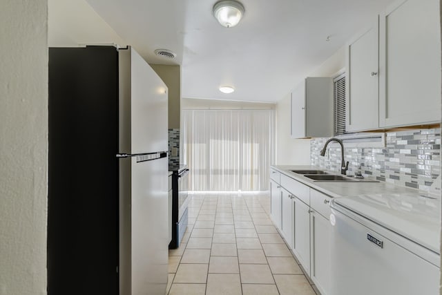 kitchen featuring dishwashing machine, sink, light tile patterned floors, stainless steel refrigerator, and white cabinets