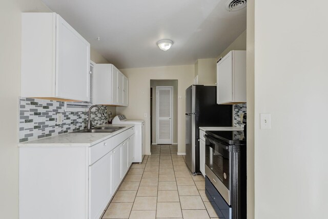 kitchen with sink, white cabinetry, light tile patterned floors, electric range, and washing machine and dryer