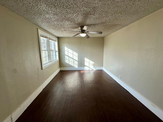 empty room featuring ceiling fan, dark wood-type flooring, and a textured ceiling