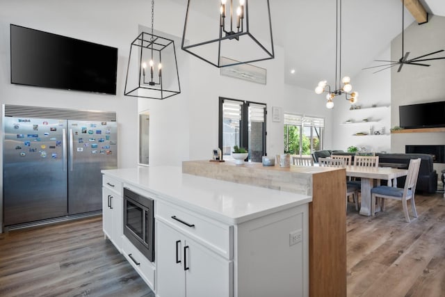 kitchen featuring pendant lighting, high vaulted ceiling, white cabinetry, a center island, and built in appliances