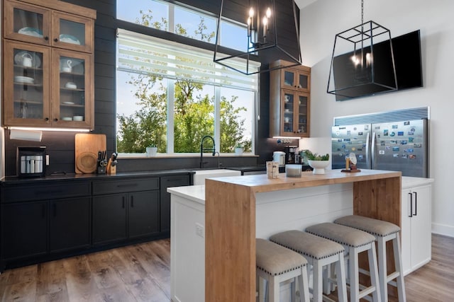 kitchen with built in fridge, sink, light wood-type flooring, and decorative light fixtures