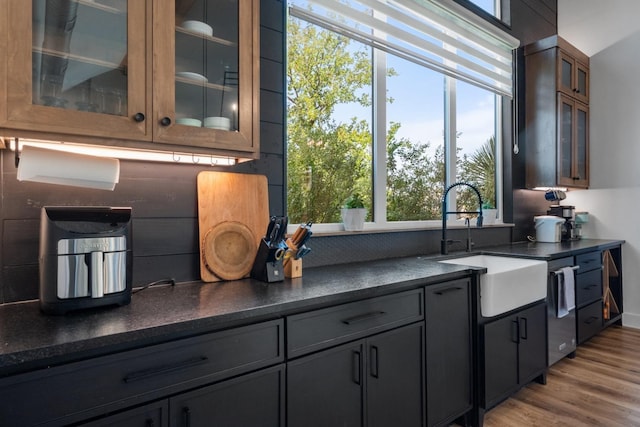 kitchen with a sink, glass insert cabinets, dark countertops, and light wood finished floors