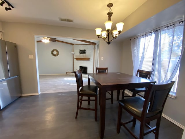 dining room featuring ceiling fan with notable chandelier, a fireplace, and dark wood-type flooring