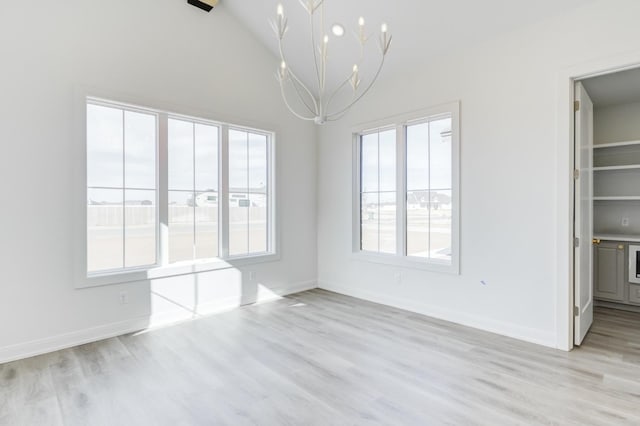 unfurnished dining area with high vaulted ceiling, a healthy amount of sunlight, an inviting chandelier, and light hardwood / wood-style floors