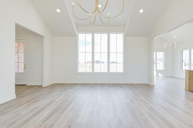 empty room with plenty of natural light, lofted ceiling, a chandelier, and light hardwood / wood-style flooring