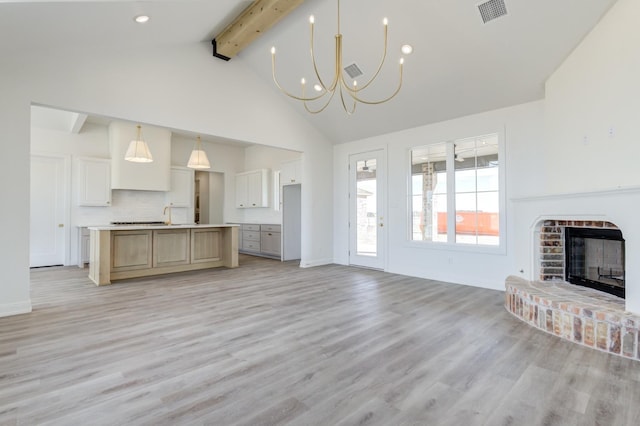 unfurnished living room featuring an inviting chandelier, a brick fireplace, light hardwood / wood-style flooring, and beamed ceiling