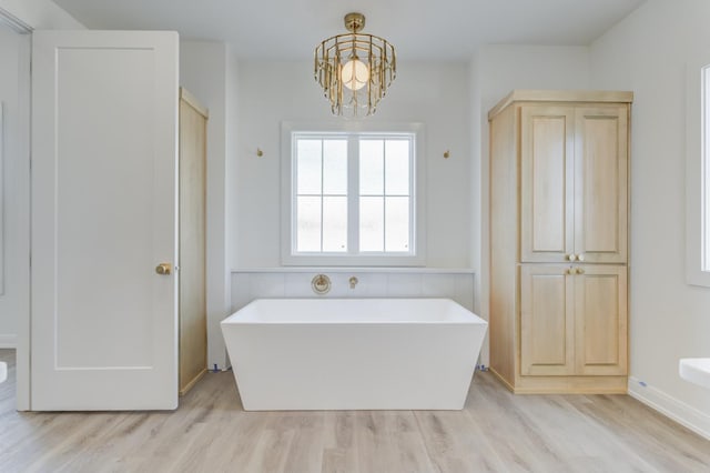 bathroom with a tub to relax in, a notable chandelier, and wood-type flooring