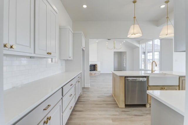 kitchen with sink, tasteful backsplash, hanging light fixtures, stainless steel dishwasher, and white cabinets