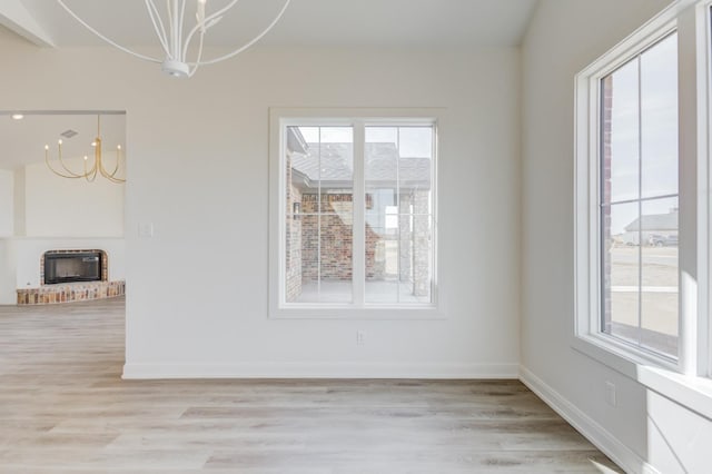 unfurnished dining area featuring an inviting chandelier, a fireplace, and light hardwood / wood-style floors