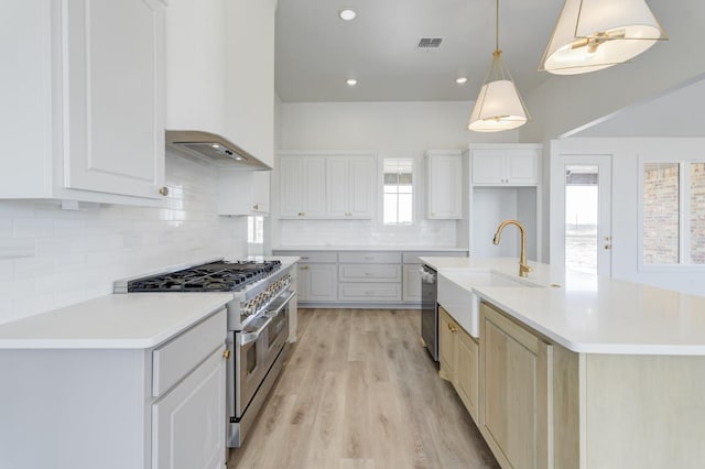 kitchen featuring premium range hood, hanging light fixtures, stainless steel appliances, an island with sink, and white cabinets