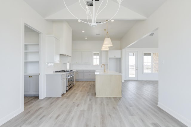 kitchen with lofted ceiling, decorative light fixtures, an island with sink, high end stove, and white cabinets