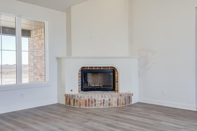 unfurnished living room with wood-type flooring and a brick fireplace