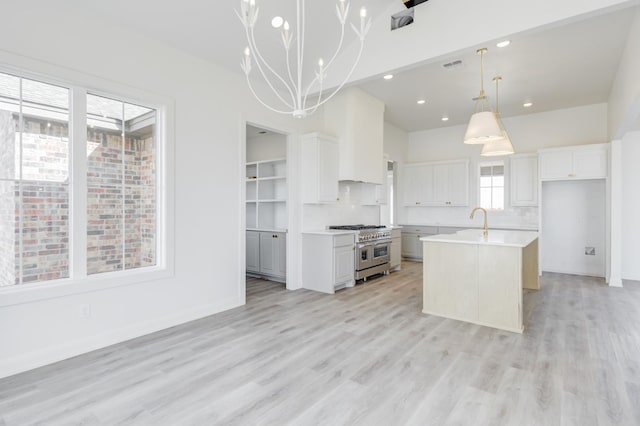 kitchen with tasteful backsplash, an island with sink, white cabinetry, range with two ovens, and hanging light fixtures