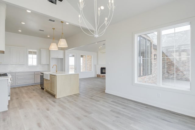 kitchen featuring dishwasher, white cabinetry, an island with sink, decorative backsplash, and vaulted ceiling