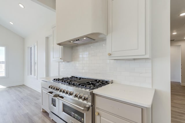 kitchen featuring premium range hood, vaulted ceiling, double oven range, light hardwood / wood-style floors, and white cabinets