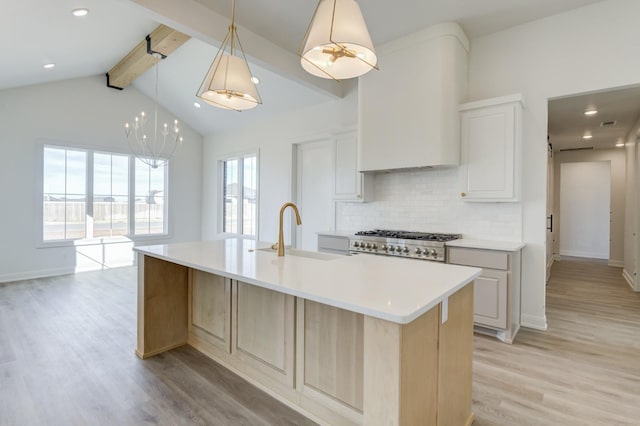 kitchen with decorative light fixtures, vaulted ceiling with beams, sink, a large island with sink, and light hardwood / wood-style floors