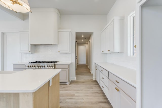 kitchen with white cabinetry, backsplash, range with two ovens, a healthy amount of sunlight, and light wood-type flooring