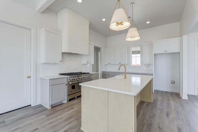 kitchen featuring a kitchen island with sink, double oven range, hanging light fixtures, and white cabinets