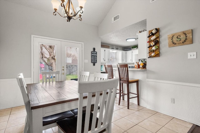 dining room featuring lofted ceiling, light tile patterned floors, french doors, and a textured ceiling